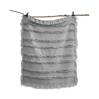 A gray fringed throw blanket hanging off a branch