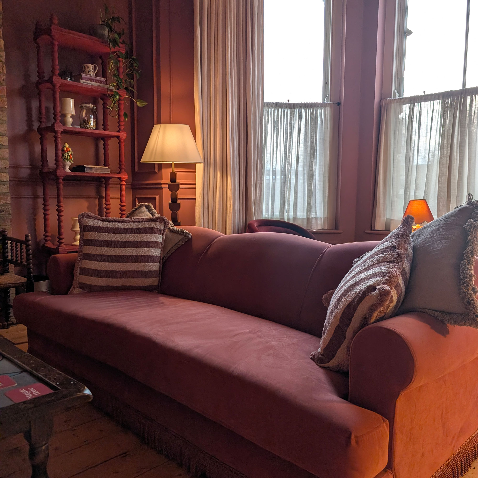 Red sofa with red and white striped cushions in front of bay window area in red panelled room