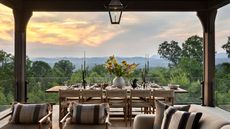 Raised back porch with armchairs and dining table framing a sunset view over the hills