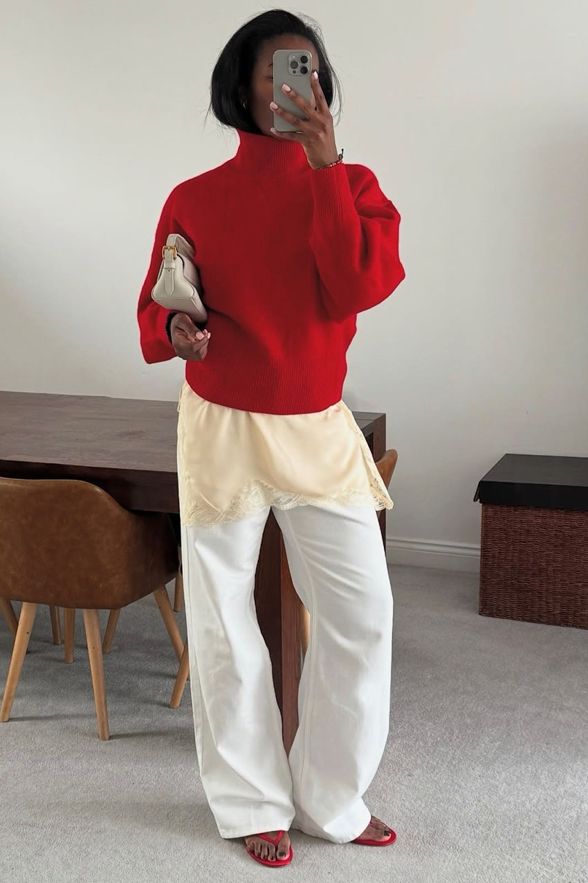 A woman wearing a red sweater, lace top, white pants, and red sandals