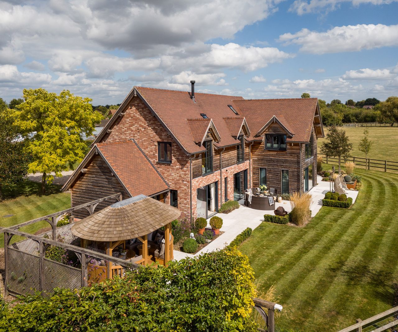 The exterior view of a timber frame self build home with red brick and timber cladding and surrounding countryside views