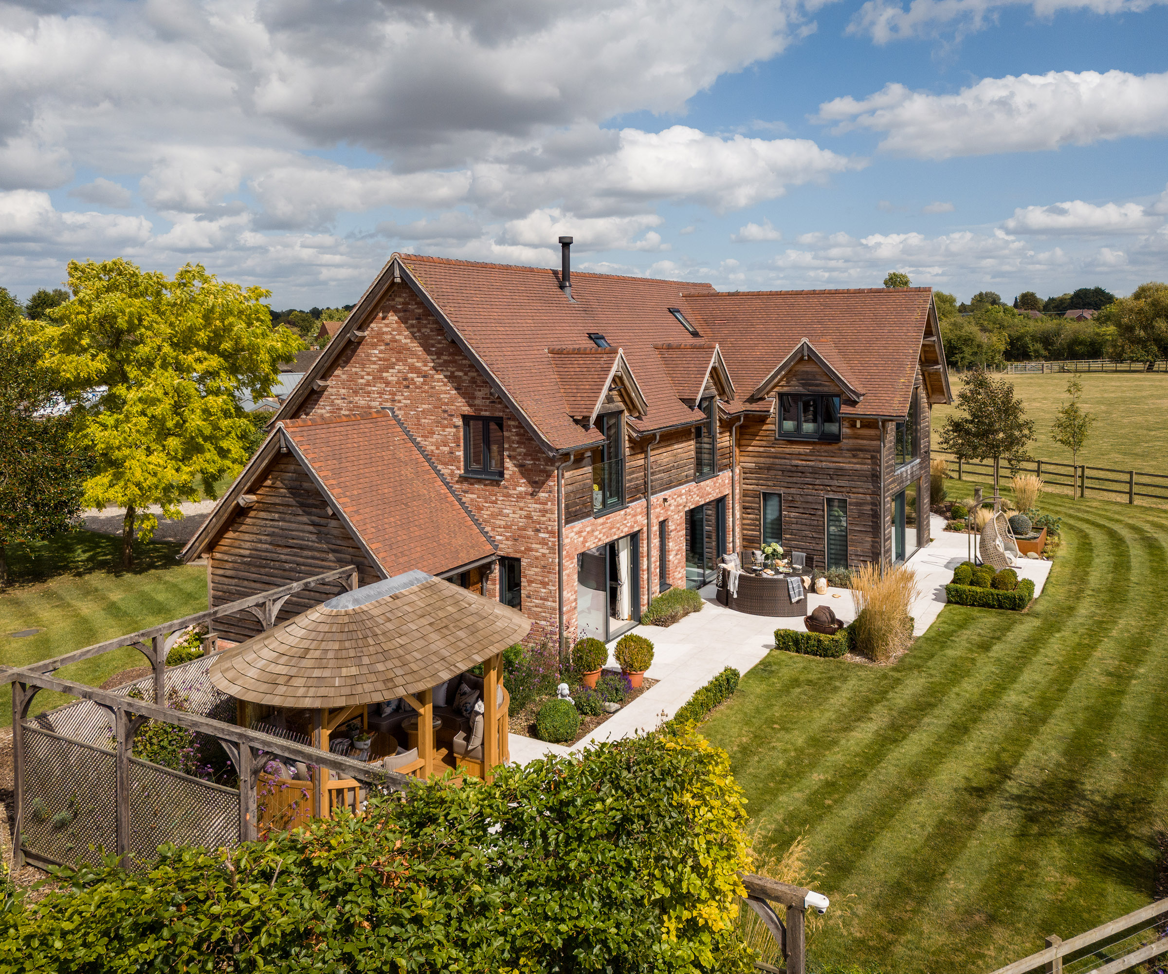 The exterior view of a timber frame self build home with red brick and timber cladding and surrounding countryside views