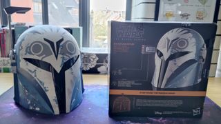 Bo-Katan helmet next to the cube-shaped box it comes in. Image in 16 by 9 format.