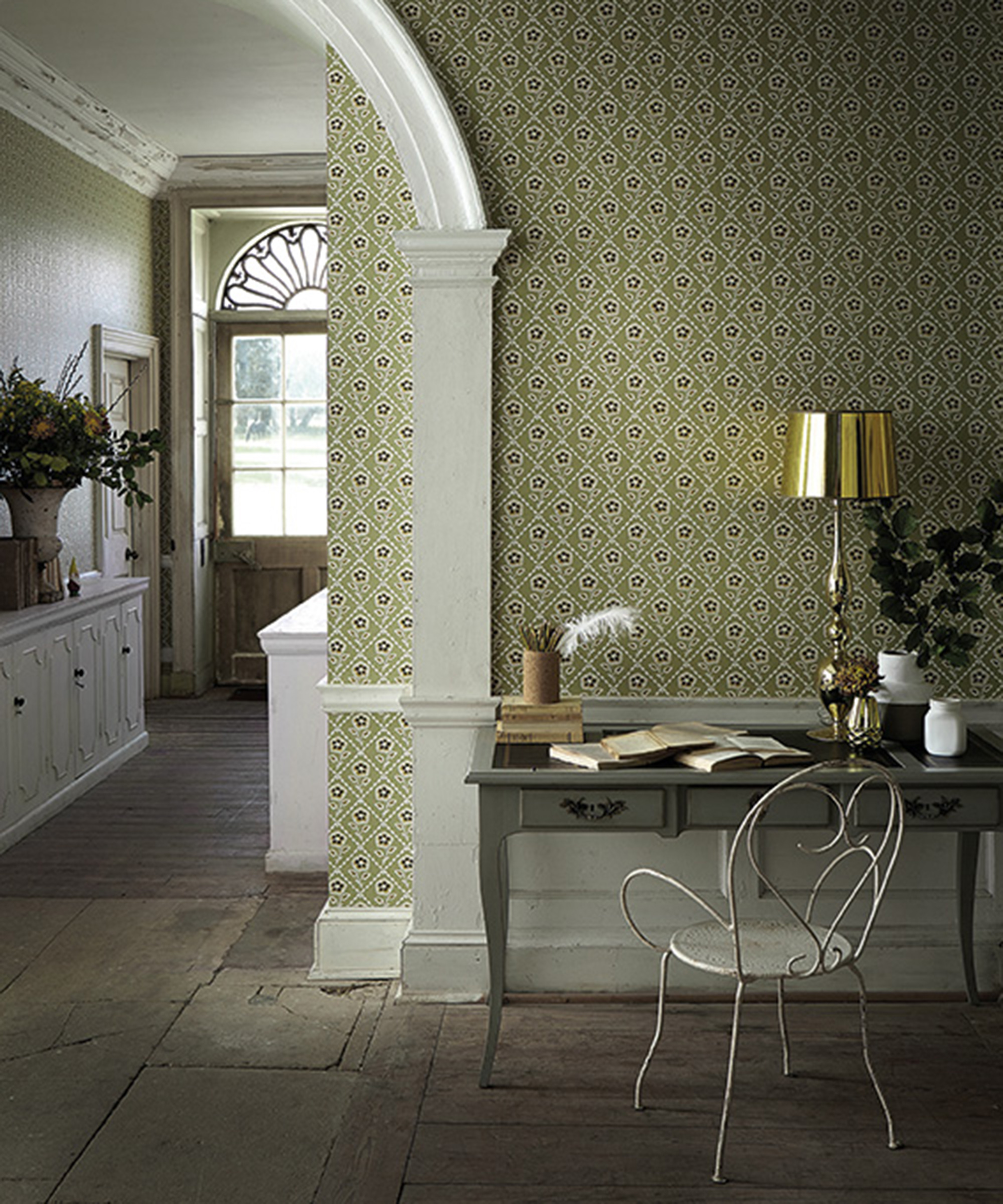 Green home office idea by Little Greene – patterned green wallpaper with a stone floor, a gray console table and small white chair, with front door in the background