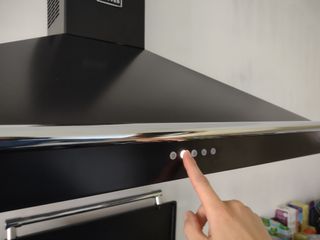 A finger pressing the buttons on the front of a black pyramid chimney cooker hood