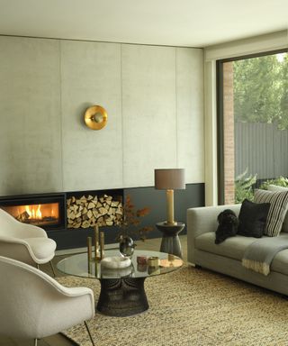 modern living room with table lamp, wall light, fireplace and sofa with two cream chairs, glass coffee table