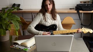 Woman playing guitar in front of her laptop