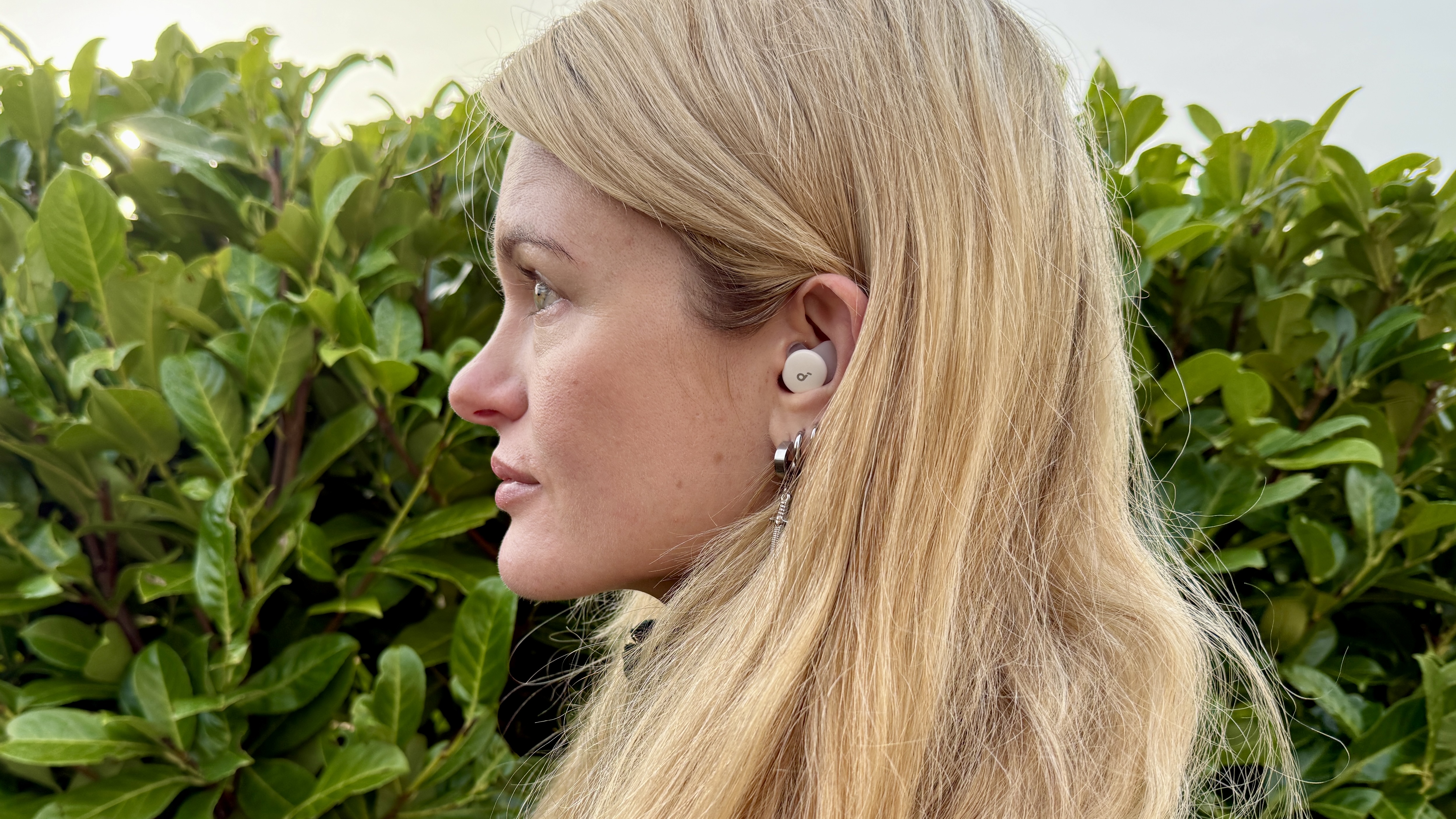 Becca Caddy wearing the soundcore sleep a30 buds against a green hedge