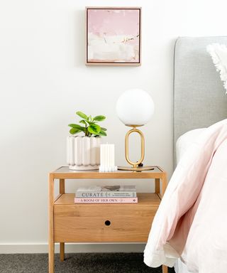 Oak modern bedside table with deep drawer, shelf, and dressed with orb lamp, scalloped candle and potted plant.