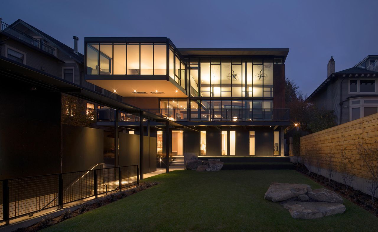 night time view from the backyard looking at a two storey house with light shining through the glass windows