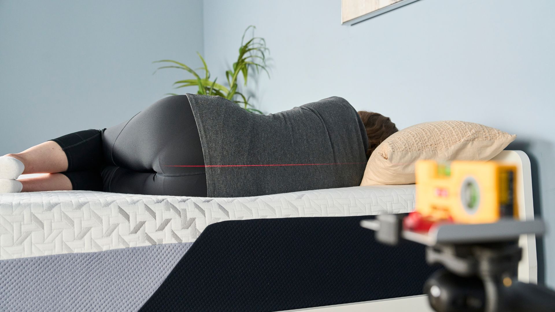 A laser pointer measures how tester Ruth Jones's spine is aligned on the Nectar Premier Memory Foam Mattress while she side sleeps.