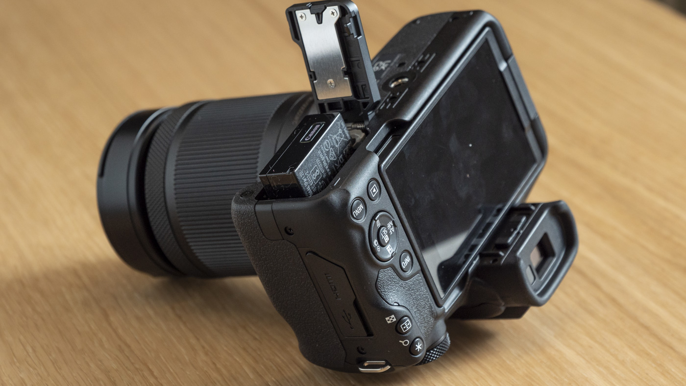Rear of Canon EOS R50 on a table upside down with battery door open and battery protruding