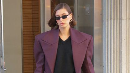 hailey bieber in a black mini skirt and oversized maroon topcoat 