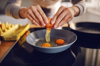Vitamin D foods: Close up of caucasian woman breaking egg and making sunny side up eggs. Domestic kitchen interior. Breakfast preparation.