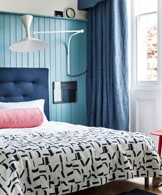Bedroom with blue wall, patterned bedlinen and wall light