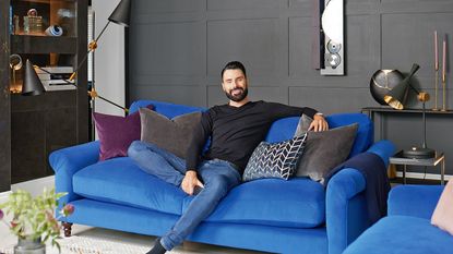 Rylan Clark in his living room standing behind his blue DFS sofa