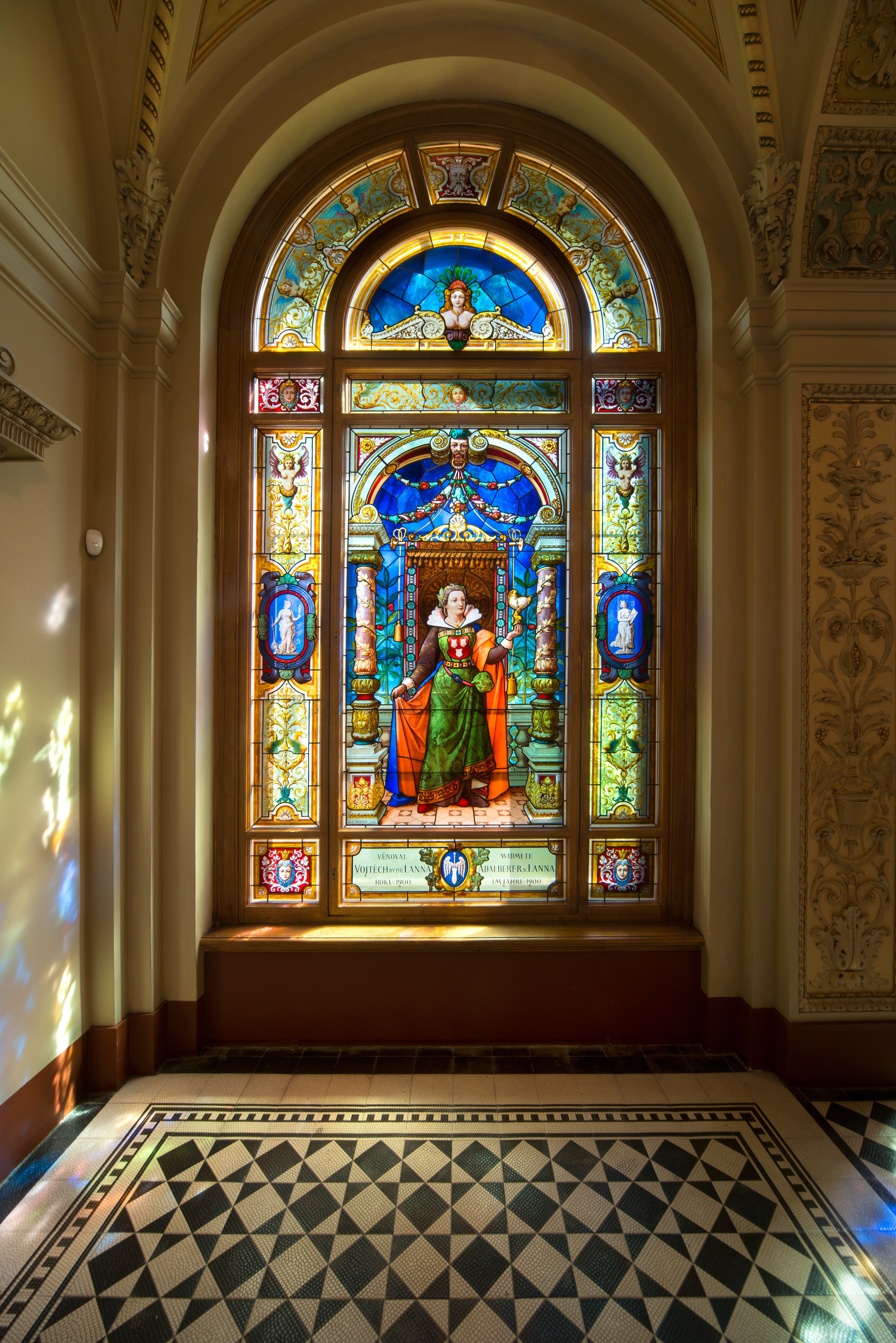 A stained glass window depicting a woman in renaissance-era clothing, placed inside a staircase with checkered floors in black and white.