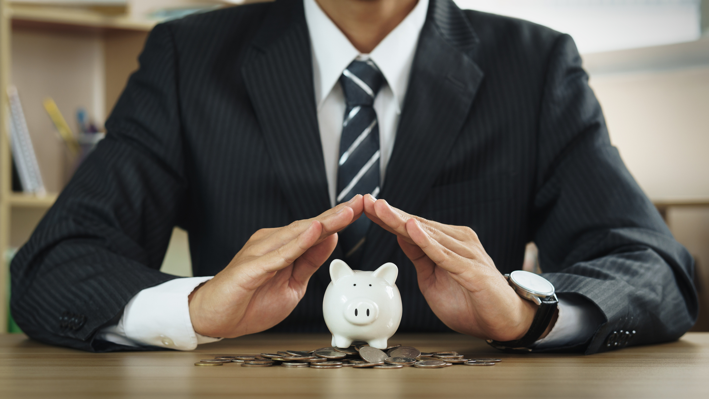 a picture of a man in a black suit holding his hands to shelter a piggy bank