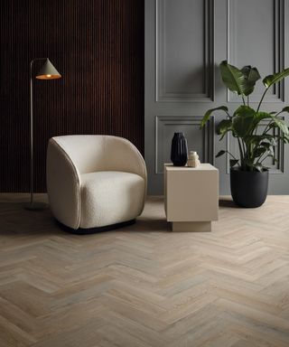 oak effect wooden vinyl floor laid in herringbone pattern with cream chair and large green plant in black pot