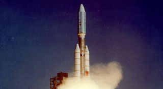 A triple-core rocket launches against a blue sky.