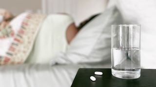 Woman lies in bed next to a glass and two pills