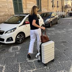 Woman wearing white pants and holding a suitcase