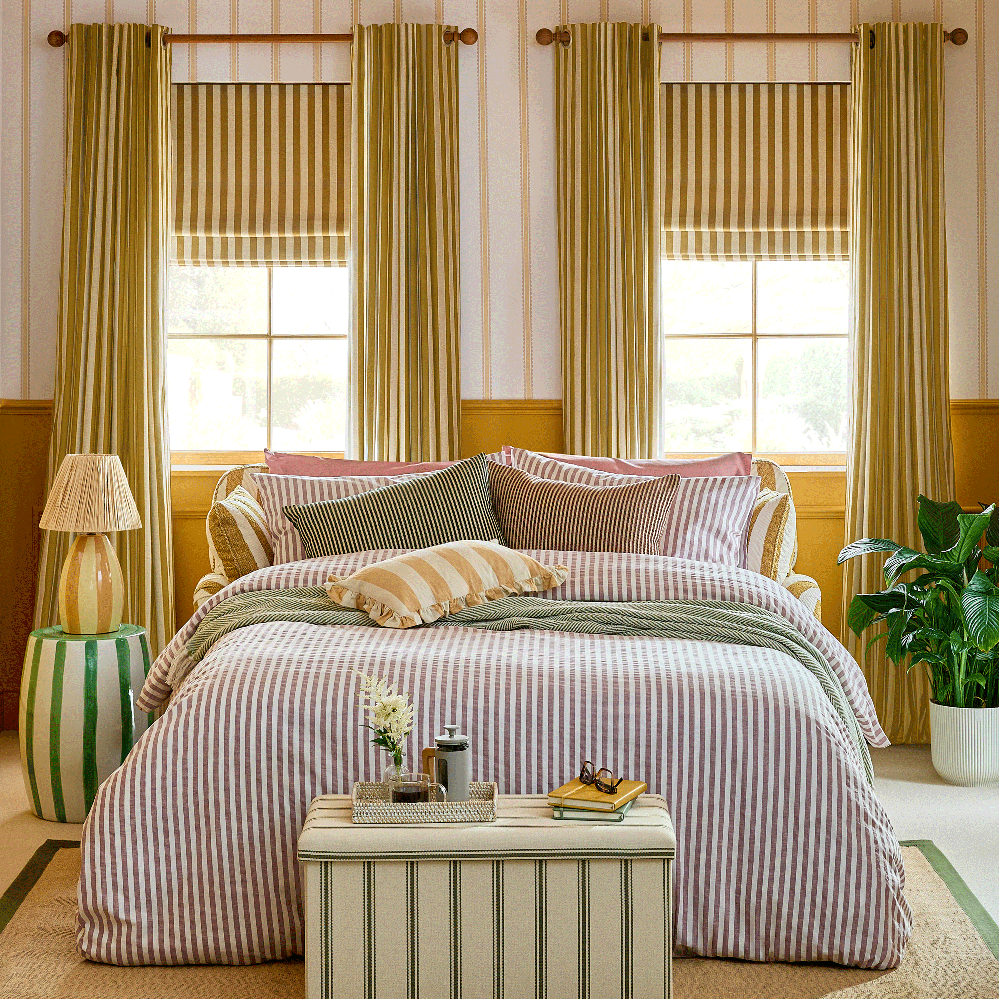 a colourful bedroom setup with an opened out sofa bed covered in striped bedlinen matching striped curtains and striped wallpaper and striped ottoman box at the end of the bed