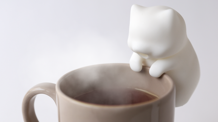 Yukai Engineering&#039;s Nékojita FuFu robot cat clipped onto the side of a steaming coffee cup