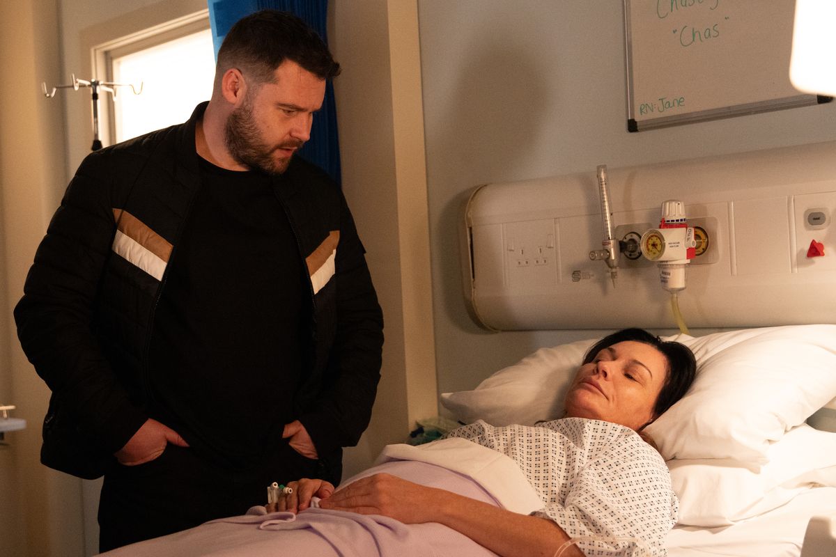 Chas Dingle lies in a hospital bed as Aaron Dingle stands over her.