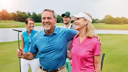 An active senior couple golfing with their adult children on a golf course.