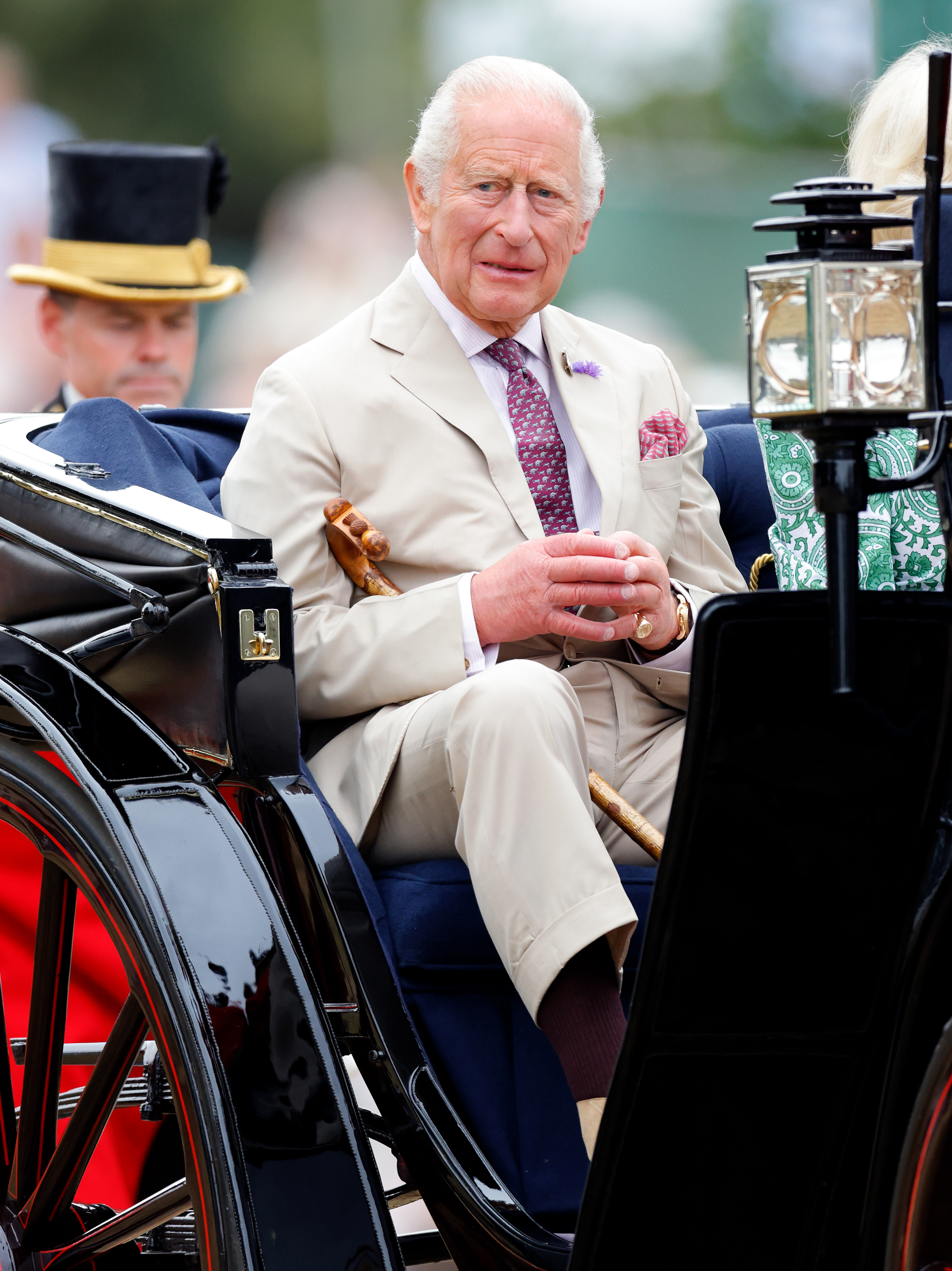 King Charles wears a light tan suit and carries a wooden walking stick while attending the RHS Sandringham Flower Show