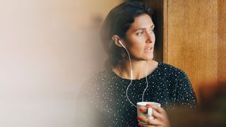 Woman stressed wearing headphones and holding coffee cup to represent habitual burnout from work