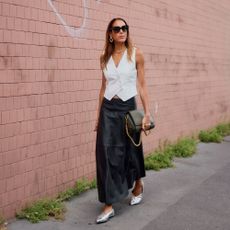 Woman wears white vest, black skirt, and silver heels. 