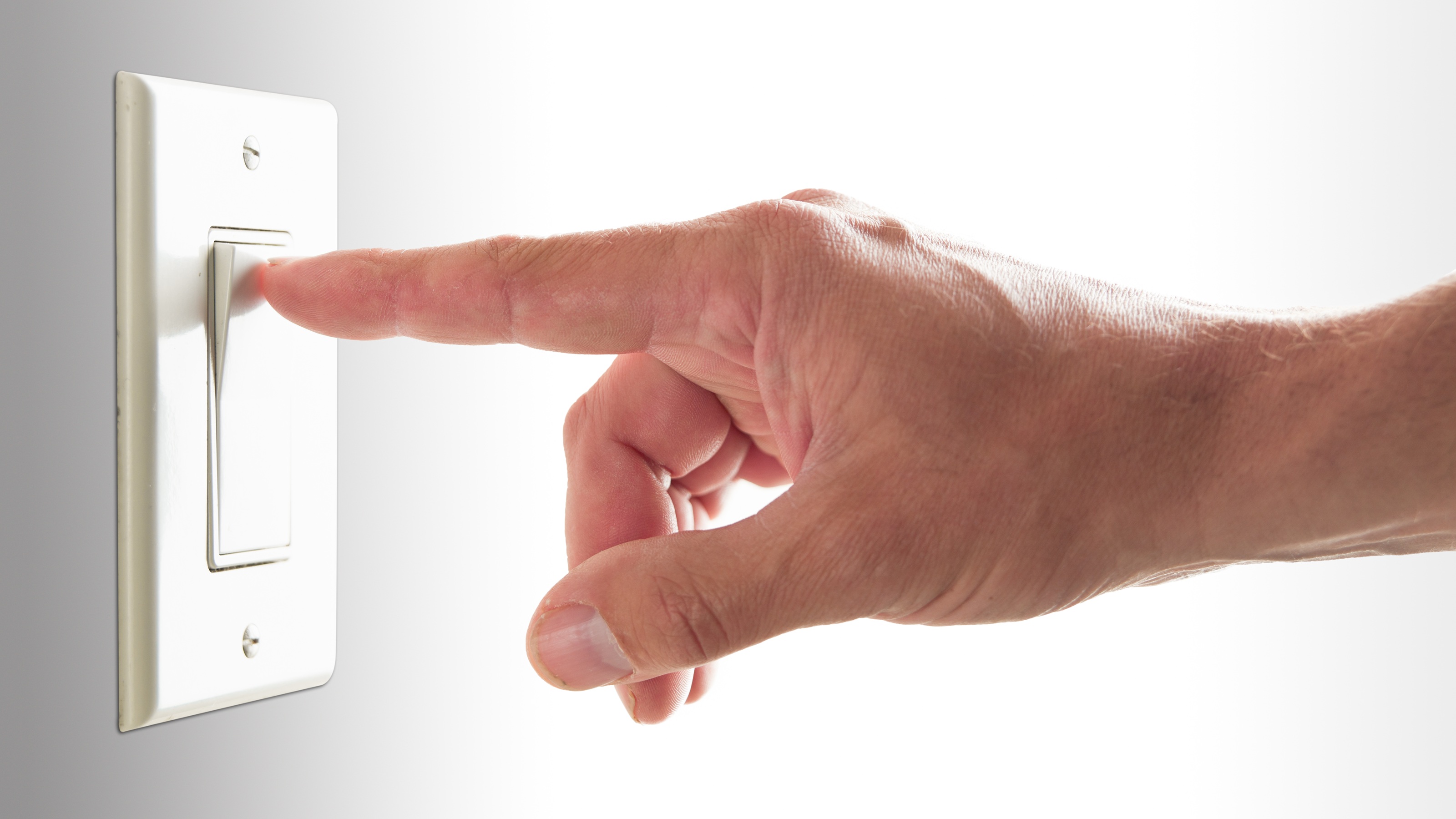 A man turns on a light switch, only his hand showing.