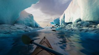 Still from the VR video game Kayak VR: Mirage. This image shows a first person view of sitting in a kayak as your paddle through blue water surrounded by icy glaciers. Just up ahead is another kayak, as well as some penguins on a high-up cliff.