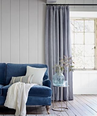 Blue gray pencil pleat curtains in living room with blue couch and white cushions