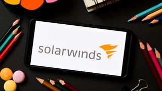 SolarWinds logo pictured on a smartphone screen with stationary items pictured surrounding.