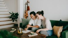 A happy couple in their late forties relax on a couch, drinking tea from Japanese cups. A guitar and ukulele hang on the wall behind them.