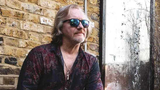 Luke Morley seated in front of a brick wall, wearing sunglasses