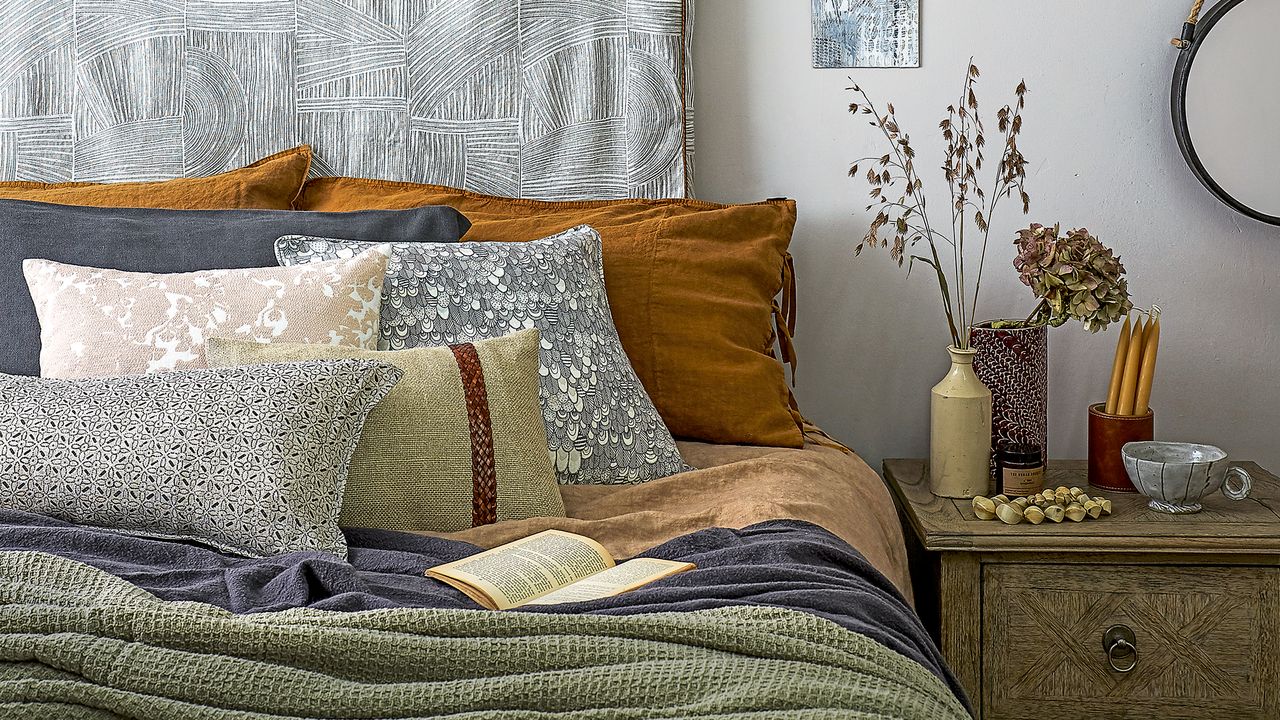 Bed with hanging headboard, piles of pillows on bed and dried flowers on bedside table