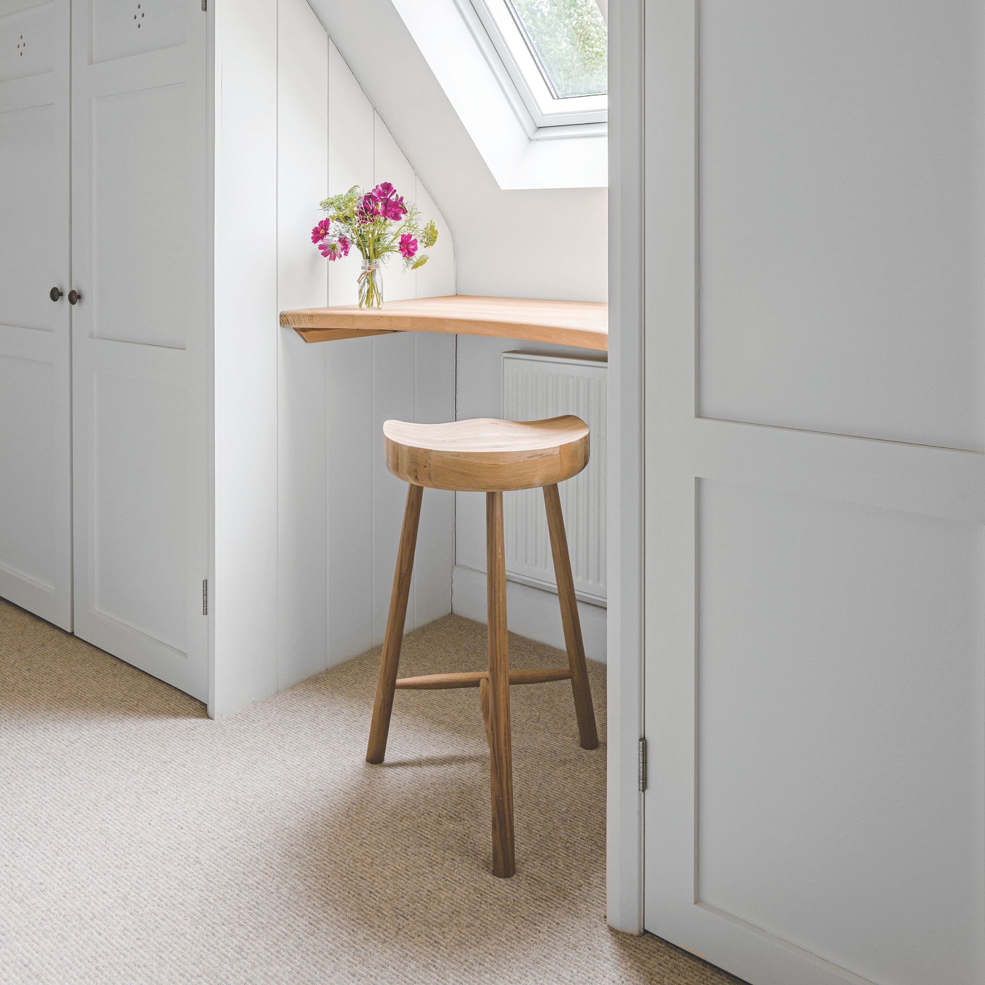 Dressing area in a loft bedroom with white wardrobes, cream carpet and a table area with a stool underneath it