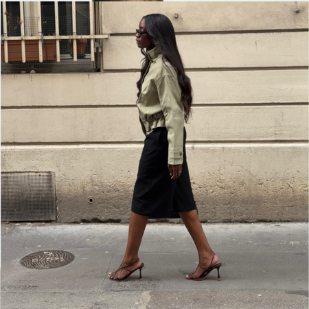 Liv wearing a funnel neck jacket, black skirt and strappy heeled sandals