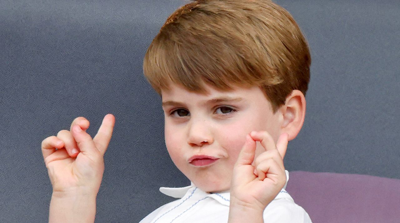 Prince Louis wears a white shirt and makes a funny face and poses with his hands