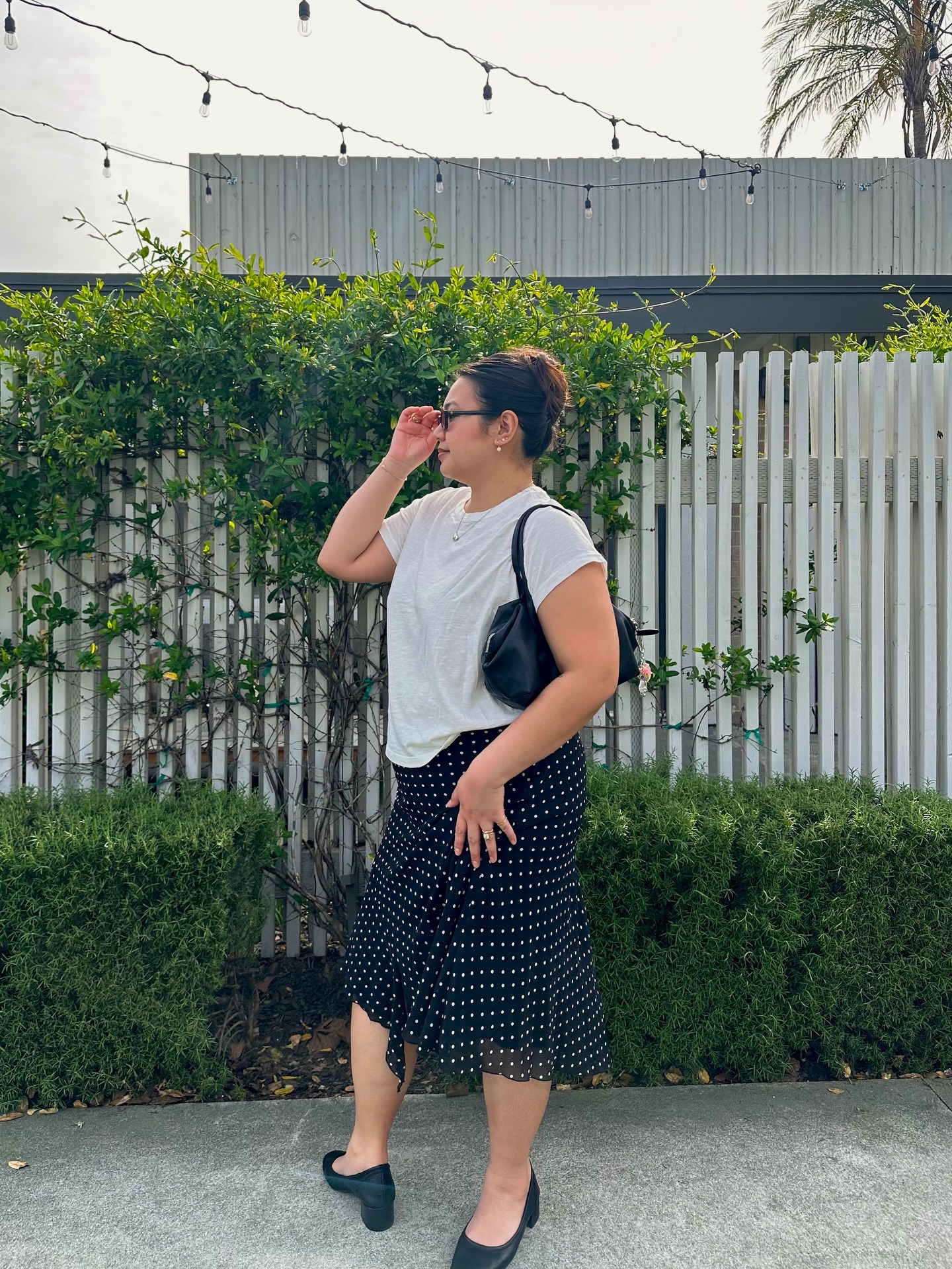 Marina wears white tee, polka dot skirt, black ballet pumps, and black handbag.