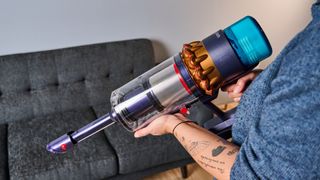 the dyson gen5detect cordless stick vacuum in prussian blue and copper, showing its cleaning head and attachment tools