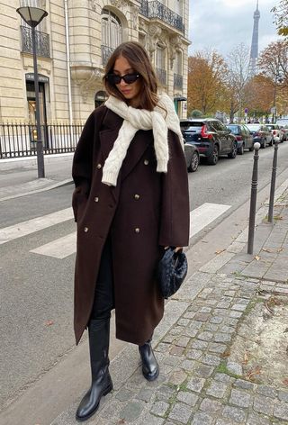 best riding boots shown in a photo of a woman in Paris wearing a brown coat over black skinny jeans with black riding boots