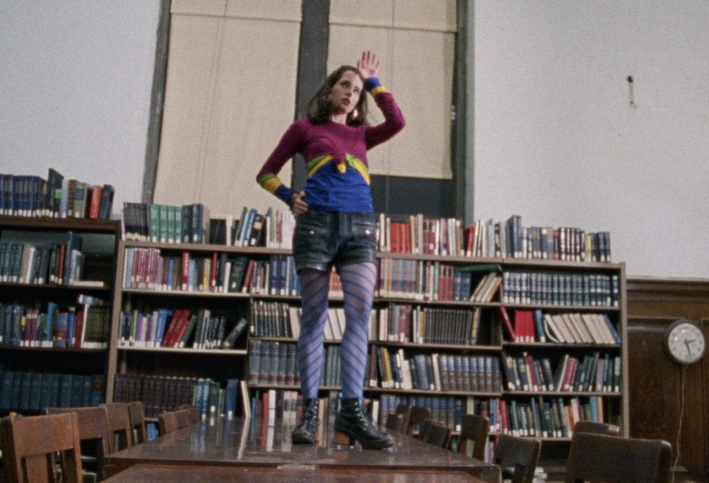 parker posey wears striped tights a jean skirt and colorful top dancing on a library table in the movie party girl