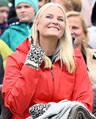 Crown Princess Mette-Marit wearing a red coat and black and white mittens looking up and smiling