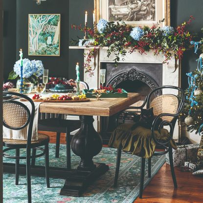 A dining room with a Christmas tree and the fireplace decorated with a floral garland and the table laden with appetisers