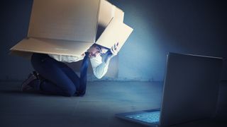 A man hiding under a cardboard box from his laptop
